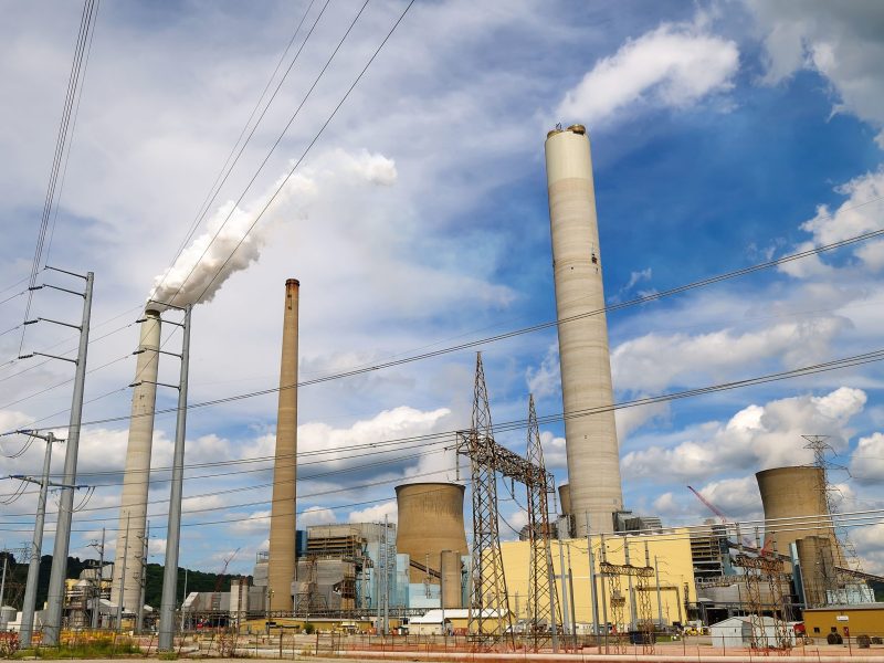 Two tall smokestacks emit white steam against a blue sky