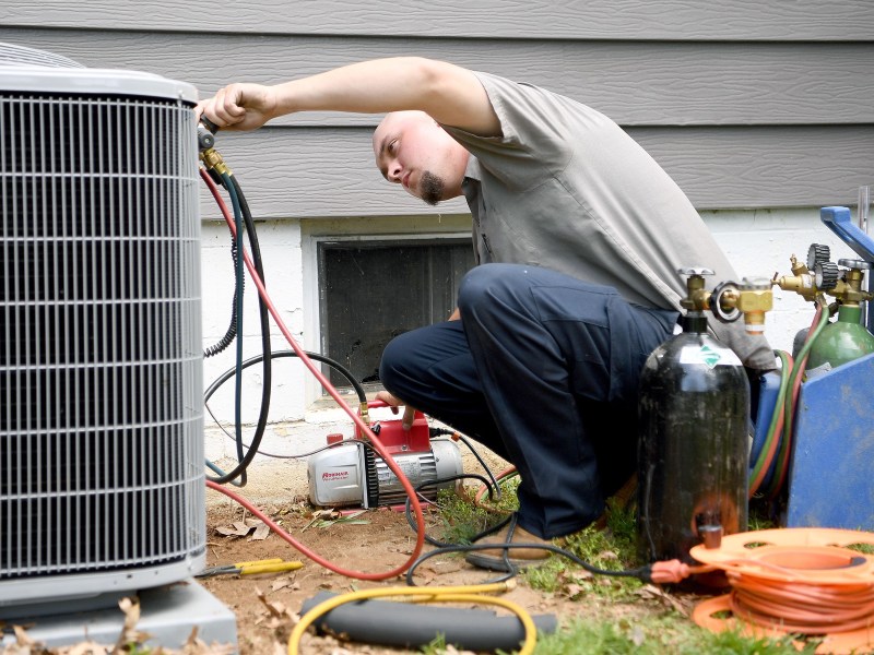 An HVAC mechanic works to change out an old furnace for a heat pump at a house.